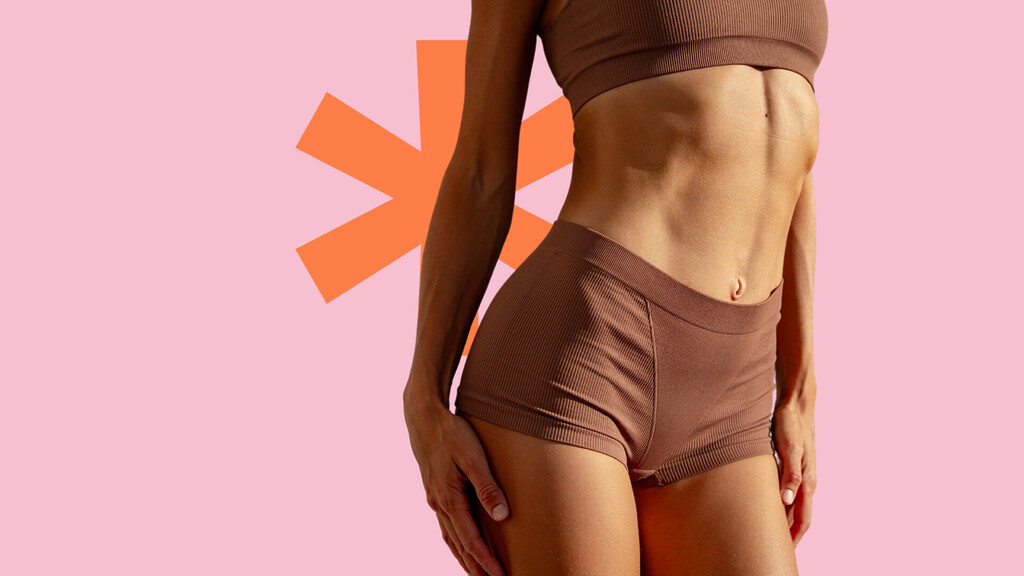 Confident woman in brown sportswear showcasing toned abdomen on a pink background, symbolizing post-baby body fitness.