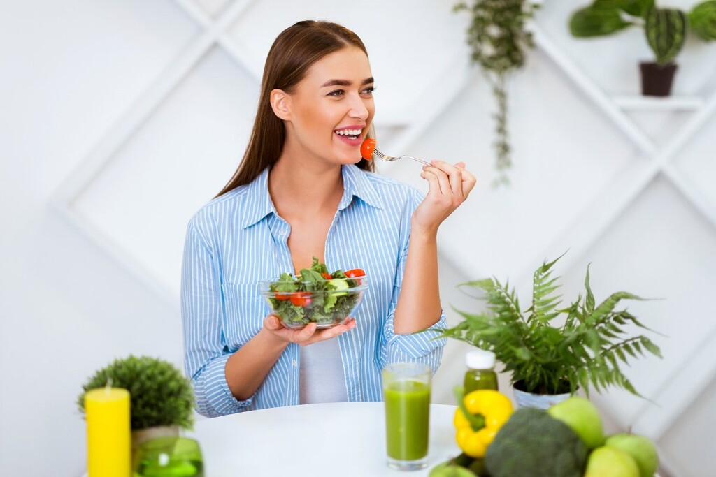 woman smiles as she eats a healthy salad with a fork